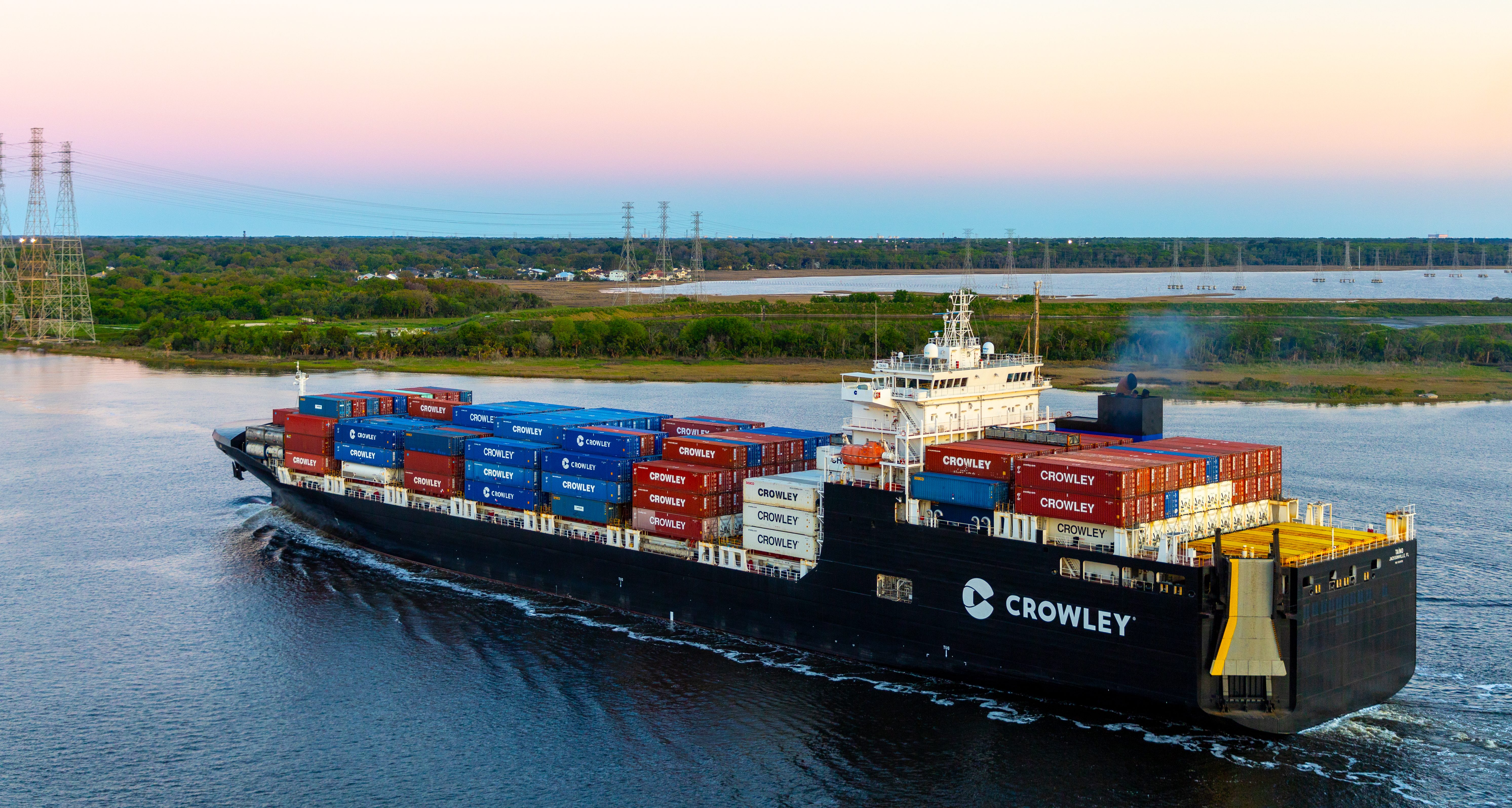 Buque de carga de Crowley navegando al atardecer con contenedores en la ruta entre Puerto Rico y Estados Unidos.
